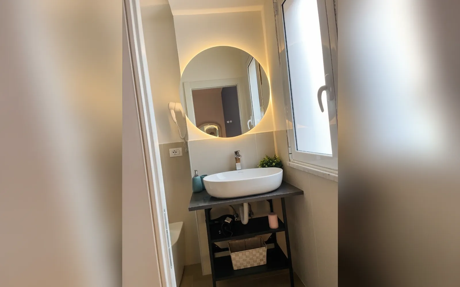 Il bagno privato con lo specchio tondo illuminato e la finestra